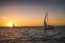 Barcos à vela flutuando no mar ondulado durante o pôr do sol cênico — Fotografia de Stock