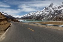 Estrada vazia, montanhas cobertas de neve e belo lago no Tibete — Fotografia de Stock