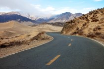 Camino de asfalto vacío y montañas durante el día, el Tíbet - foto de stock
