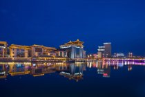 Illuminated buildings reflected in calm water at night, Dunhuang desert, Gansu — Stock Photo