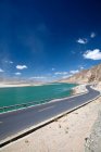 Camino de asfalto vacío, lago y montañas en el día soleado, Tíbet - foto de stock