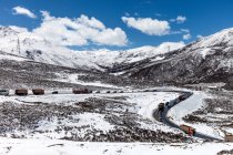 Vista de ángulo alto de los coches y camiones en la carretera sinuosa entre hermosas montañas cubiertas de nieve - foto de stock