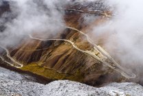 Повітряний вид на звивисту дорогу в мальовничих горах, вкритих хмарами — стокове фото