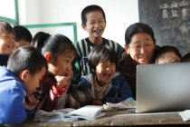 Profesora rural y alumnas usando ordenador portátil juntas en la escuela - foto de stock