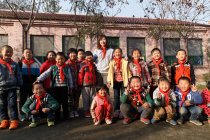 Profesora rural y alumnas chinas felices de pie juntas en el patio de la escuela - foto de stock