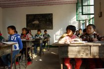 Орієнтовані студенти китайської школи сидять на столах і навчання в сільській початкової школи — стокове фото