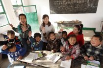 Высокий угол обзора сельской учительницы и китайских учеников, улыбающихся перед камерой в классе — стоковое фото