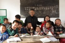 Male teacher and chinese pupils smiling at camera in classroom — Stock Photo