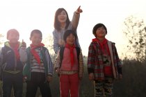 Maestra rural señalando con el dedo para estudiantes chinos de pie al aire libre - foto de stock