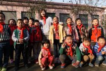 Сельская учительница и счастливые китайские ученики стоят перед школой и улыбаются перед камерой — стоковое фото