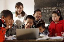 Сільська вчителька та учні з використанням ноутбука разом у класі — стокове фото
