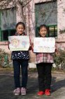 Grundschüler halten Zeichnungen hoch und lächeln in die Kamera auf dem Schulhof — Stockfoto