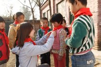 Profesor chino rural y alumnos en pañuelos rojos en el patio de la escuela - foto de stock