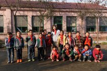 Professor rural feminino e alunos chineses felizes em pé juntos no pátio da escola — Fotografia de Stock