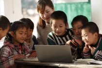 Profesora rural y alumnas chinas utilizando ordenadores portátiles juntas en la escuela - foto de stock