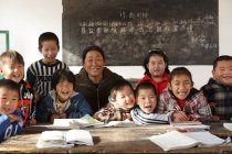 Rural female teacher and chinese pupils smiling at camera in the classroom — Stock Photo