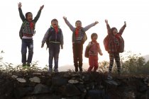 Felices alumnos chinos rurales levantando brazos y animando al aire libre - foto de stock