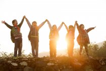 Счастливые сельские ученики держатся и поднимают руки, стоя на холме на рассвете — стоковое фото
