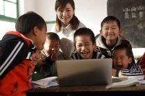 Сільська вчителька та учні з використанням ноутбука разом у класі — стокове фото