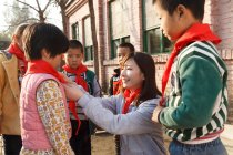 Profesor chino rural y alumnos en pañuelos rojos en el patio de la escuela - foto de stock