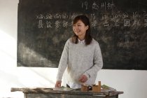 Happy chinese rural female teacher standing near chalkboard in classroom — Stock Photo