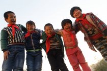 Низкий угол зрения счастливых китайских учеников, стоящих вместе и улыбающихся в камеру на открытом воздухе — стоковое фото