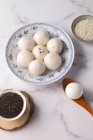 Вид зверху на клейові рисові кульки на тарілці та насіння кунжуту в мисках — стокове фото