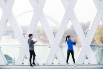 Side view of sporty young asian couple of joggers stretching together on bridge — Stock Photo