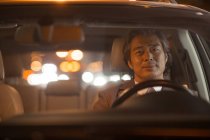 Blick durch die Windschutzscheibe eines reifen asiatischen Mannes, der nachts Auto fährt und in die Kamera lächelt — Stockfoto