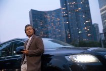 Низький кут зору зрілого азіатського чоловіка, що стоїть біля автомобіля і використовує смартфон — стокове фото