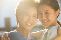 Glückliche Mutter mit erwachsener Tochter, die sich umarmt und im Freien in die Kamera lächelt — Stockfoto