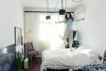 Beautiful happy young asian woman in pajamas jumping on bed — Stock Photo