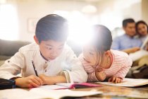 Entzückende chinesische Kinder, die zu Hause Hausaufgaben machen, Eltern, die hinter ihnen sitzen — Stockfoto