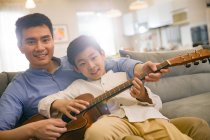 Glücklicher chinesischer Vater und Sohn spielen zu Hause gemeinsam Akustikgitarre — Stockfoto