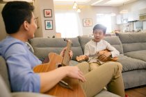 Feliz asiático pai e filho tocando guitarras juntos em casa — Fotografia de Stock