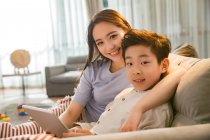 Happy mother with son using digital tablet and smiling at camera together at home — Stock Photo