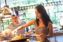 Glückliches junges asiatisches Paar hält Teller in der Hand und wählt köstliches Essen am Buffet — Stockfoto