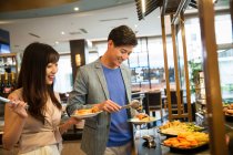 Feliz joven asiático pareja elegir delicioso comida en buffet - foto de stock