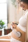Cropped shot of smiling young pregnant woman holding headphones on belly — Stock Photo