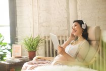 Sorridente giovane donna incinta in cuffia utilizzando tablet digitale a casa — Foto stock