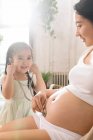 Adorable enfant souriant tenant stéthoscope et écoutant le ventre de la mère enceinte — Photo de stock