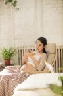 Sorridente giovane donna incinta seduta in poltrona e utilizzando smartphone a casa — Foto stock