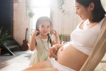 Очаровательный ребенок со стетоскопом играет с беременной матерью — стоковое фото
