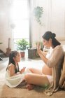 Side view of happy young pregnant woman playing with adorable little daughter at home — Stock Photo