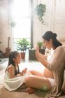 Side view of happy young pregnant woman playing with adorable little daughter at home — Stock Photo