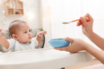 Cropped shot of mother holding spoon and feeding adorable infant baby — Stock Photo
