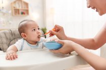 Schnappschuss einer lächelnden jungen Mutter, die ihr entzückendes Baby zu Hause füttert — Stockfoto
