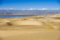 Dune di sabbia, corpo d'acqua e montagne all'orizzonte nella giornata di sole — Foto stock