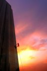 Visão de baixo ângulo do limpador de vidro trabalhando fora do arranha-céu durante o nascer do sol — Fotografia de Stock