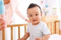 Adorable happy asian baby boy sitting in crib and looking at camera — Stock Photo